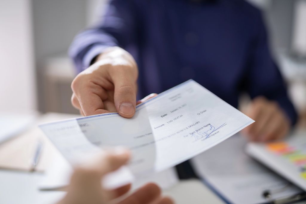 Hands Handing Check To Another Person At Desk